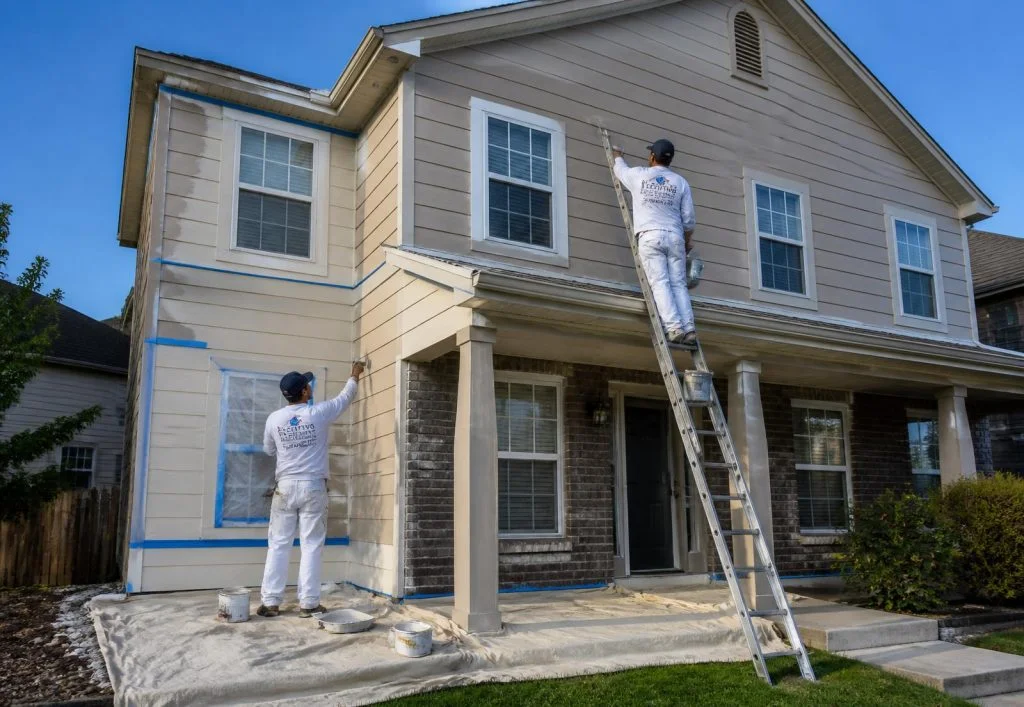 Painters applying exterior paint to two-story house with fiber cement siding and brick foundation
